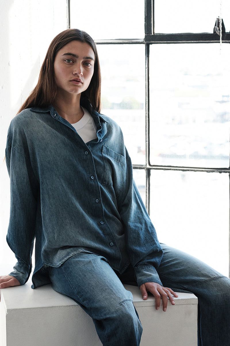 TBS EXCLUSIVE Stonewashed Chambray Oversized Shirt in Medium Wash-model leaning and sitting by a window