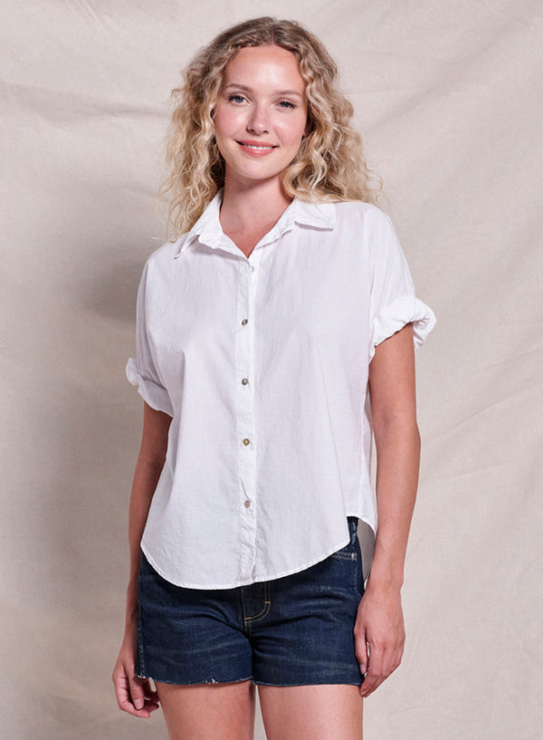 Woman wearing a white shirt and denim shorts against a beige background