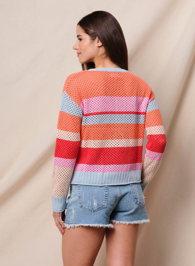 Woman wearing a colorful striped sweater and denim shorts against a neutral background.